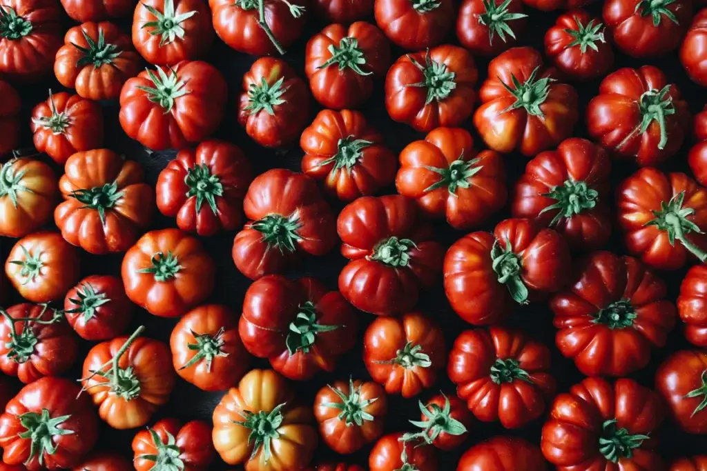 A close-up view of a variety of ripe, red heirloom tomatoes arranged closely together, showcasing their unique shapes and vibrant colors against a dark background.