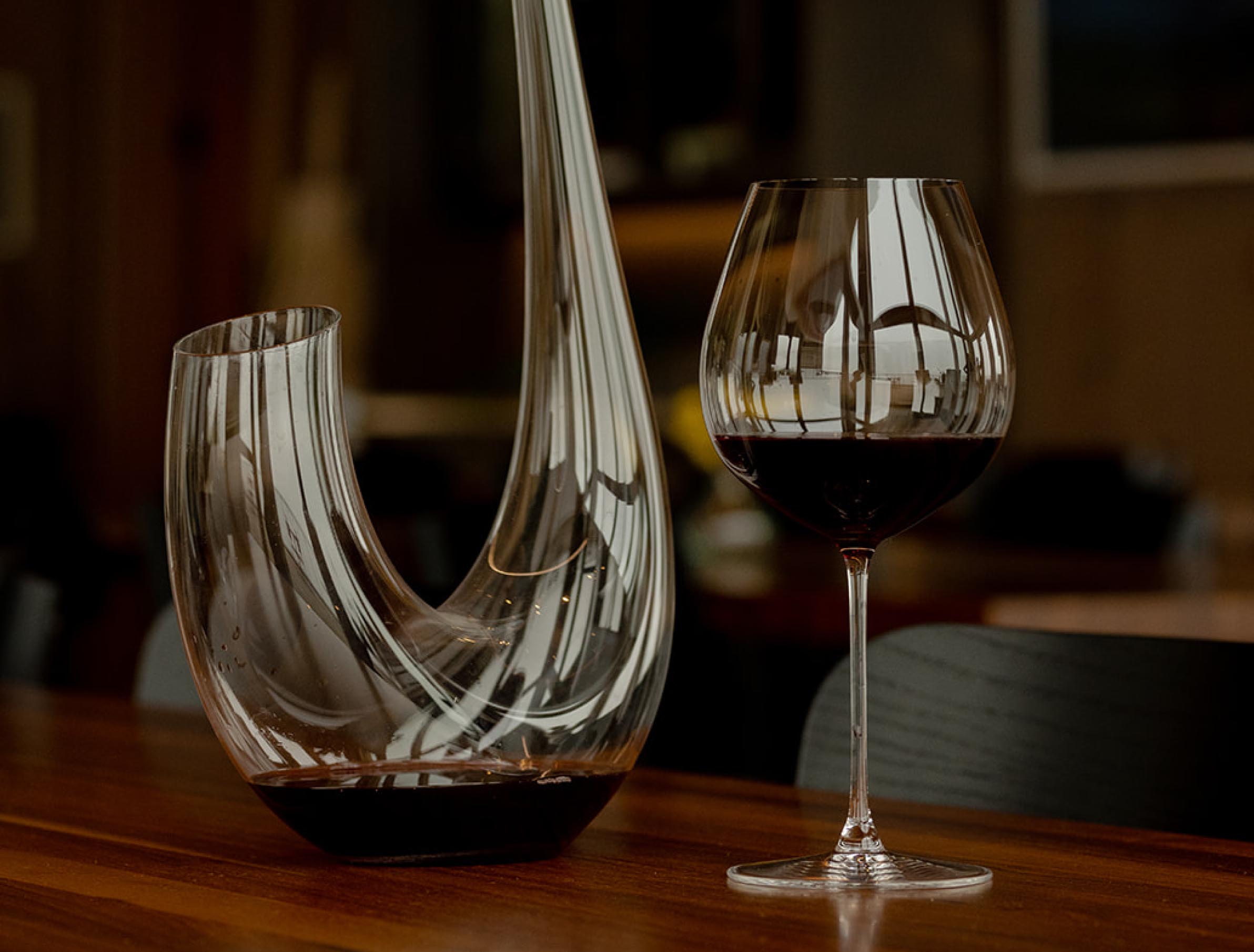 Elegant glass wine decanter and a filled wine glass on a wooden table, showcasing luxury dining and wine appreciation.