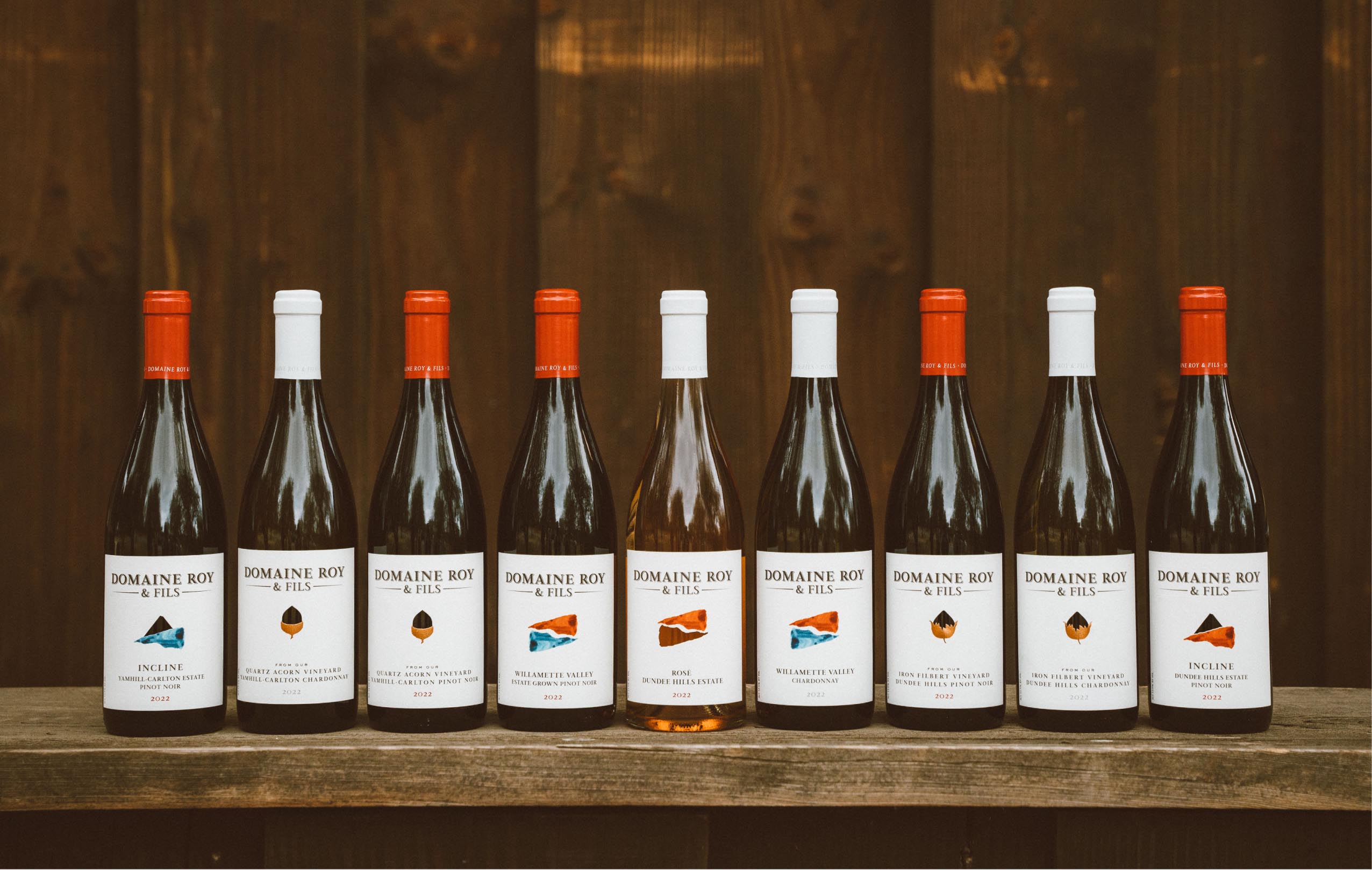 A selection of eight wine bottles displayed on a wooden shelf, featuring various labels and colors, showcasing a range of white wines with distinctive caps and branding.