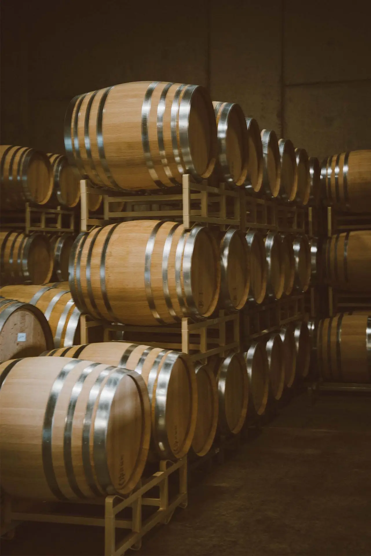 Wooden wine barrels stacked neatly in a dimly lit winery, showcasing the craftsmanship of barrel aging in wine production.